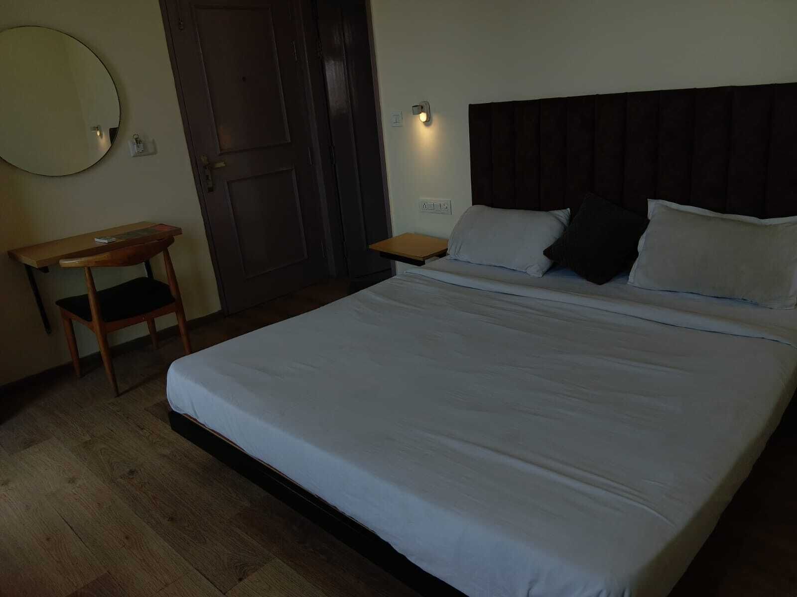 A neatly arranged bedroom with a bed, a wooden nightstand, a small table, and a wall-mounted light.
