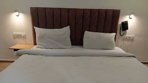 A neatly made bed with white linens and two pillows, a wooden nightstand with a lamp, and a wall-mounted telephone.