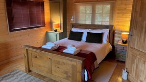 A wooden cabin bedroom with a bed, bedside lamps, and a window with blinds.
