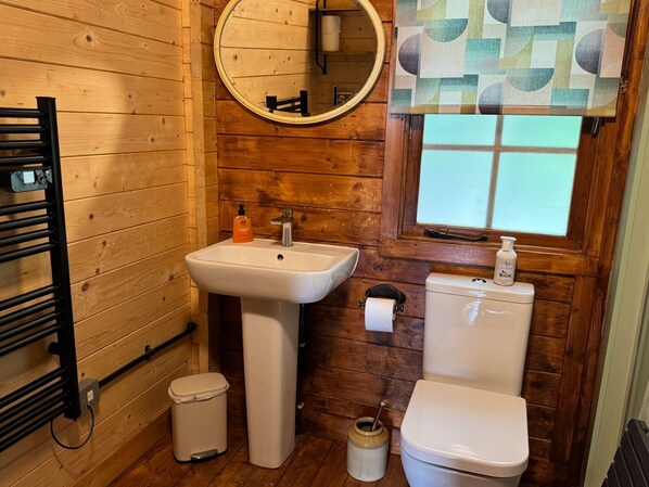 A wooden-paneled bathroom with a white sink, toilet, and a small trash bin. - Rudley Ranch (Waterlooville)