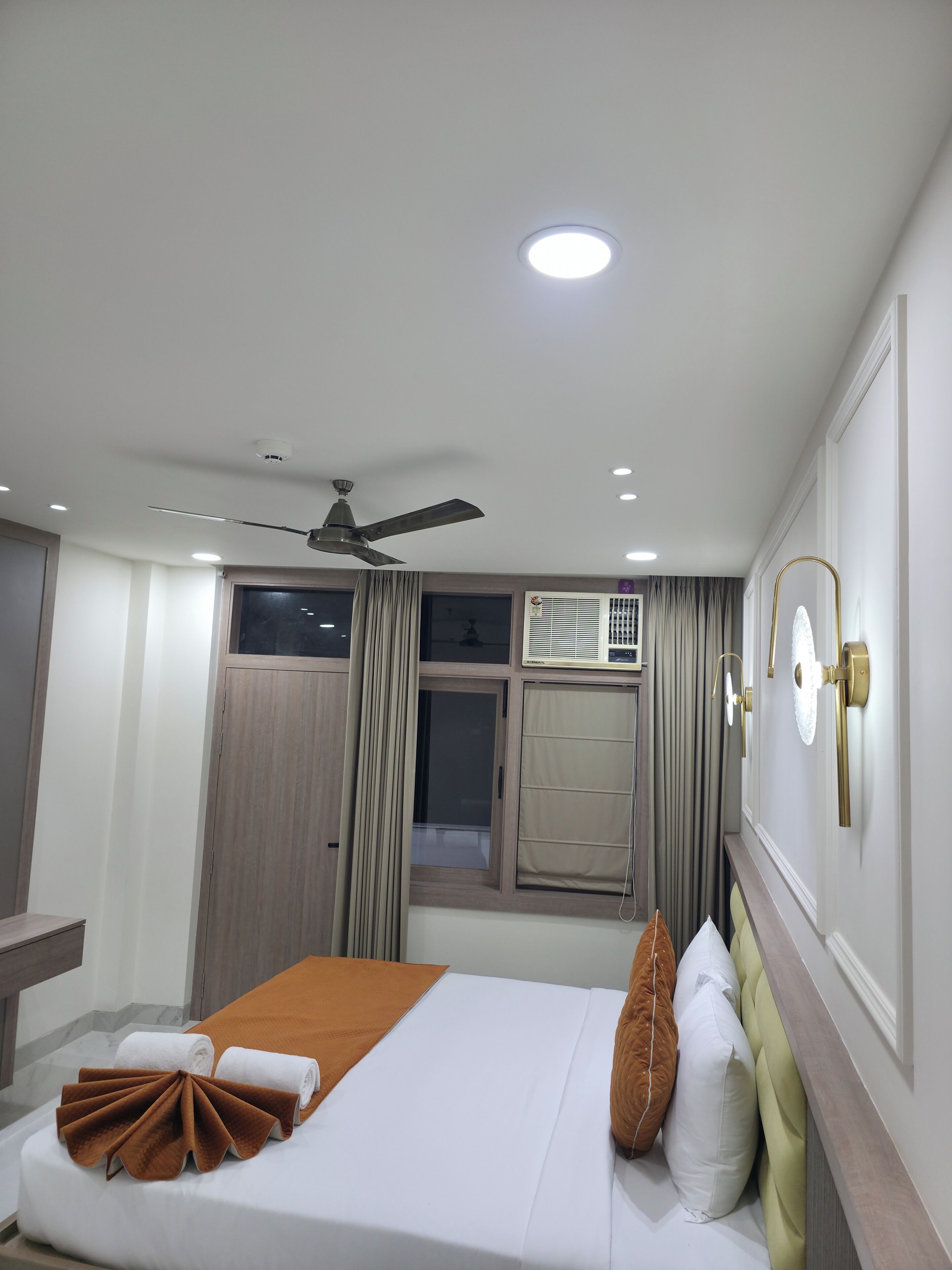 A hotel room with a bed, a ceiling fan, a window with curtains, and a wall-mounted air conditioning unit.