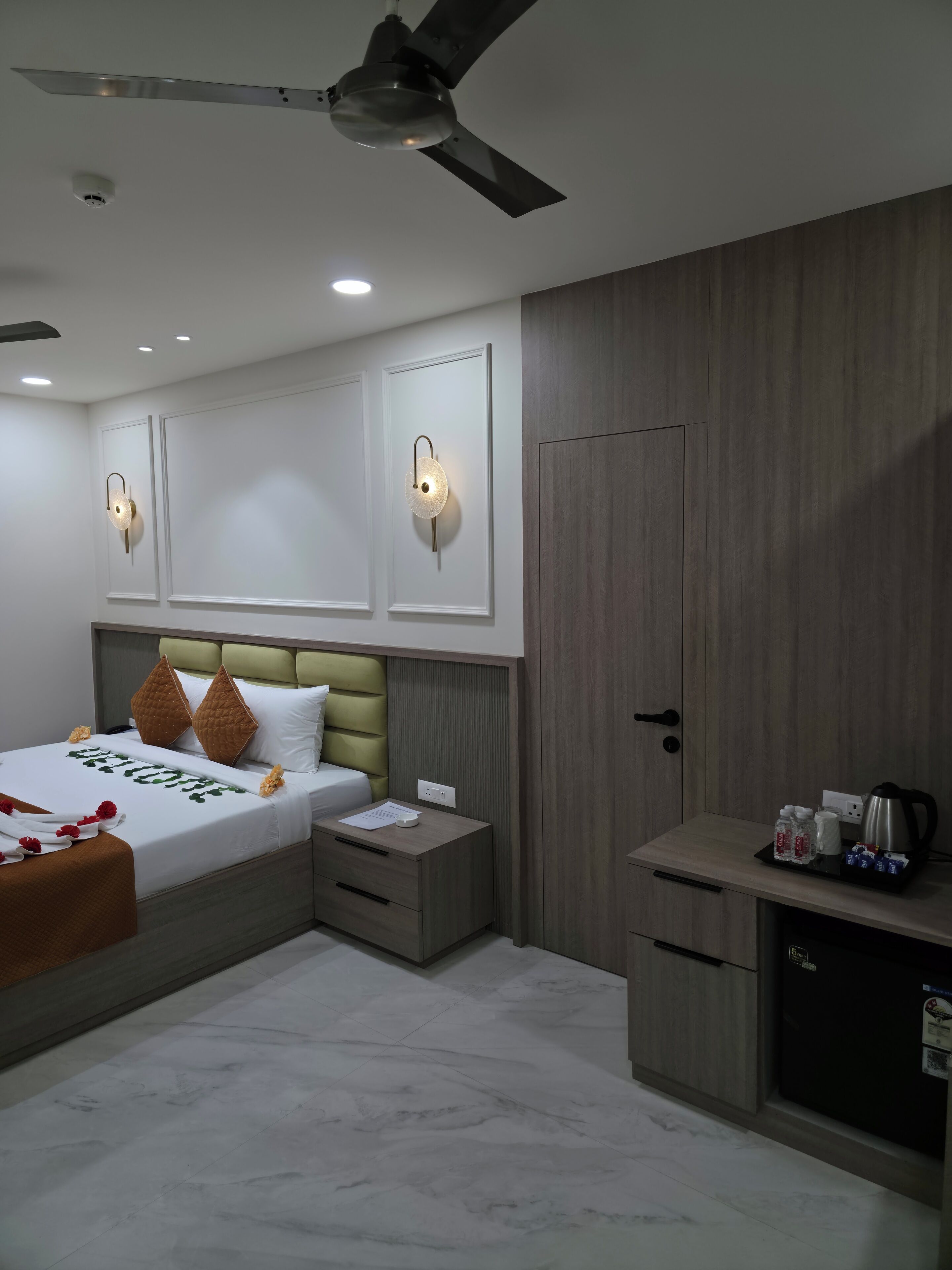 A modern hotel room with a bed, bedside tables, a desk, and a ceiling fan.