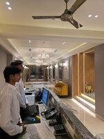 A modern hotel lobby with a reception desk, computers, a chandelier, and a ceiling fan.