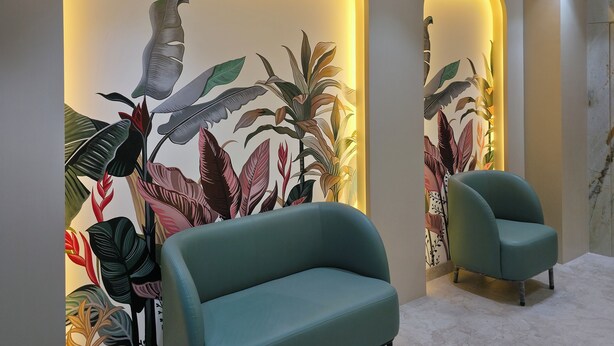 A modern living room with a teal sofa, a ceiling fan, and a wall mural with tropical leaves and birds. - Bawa Hotel (Kanpur)