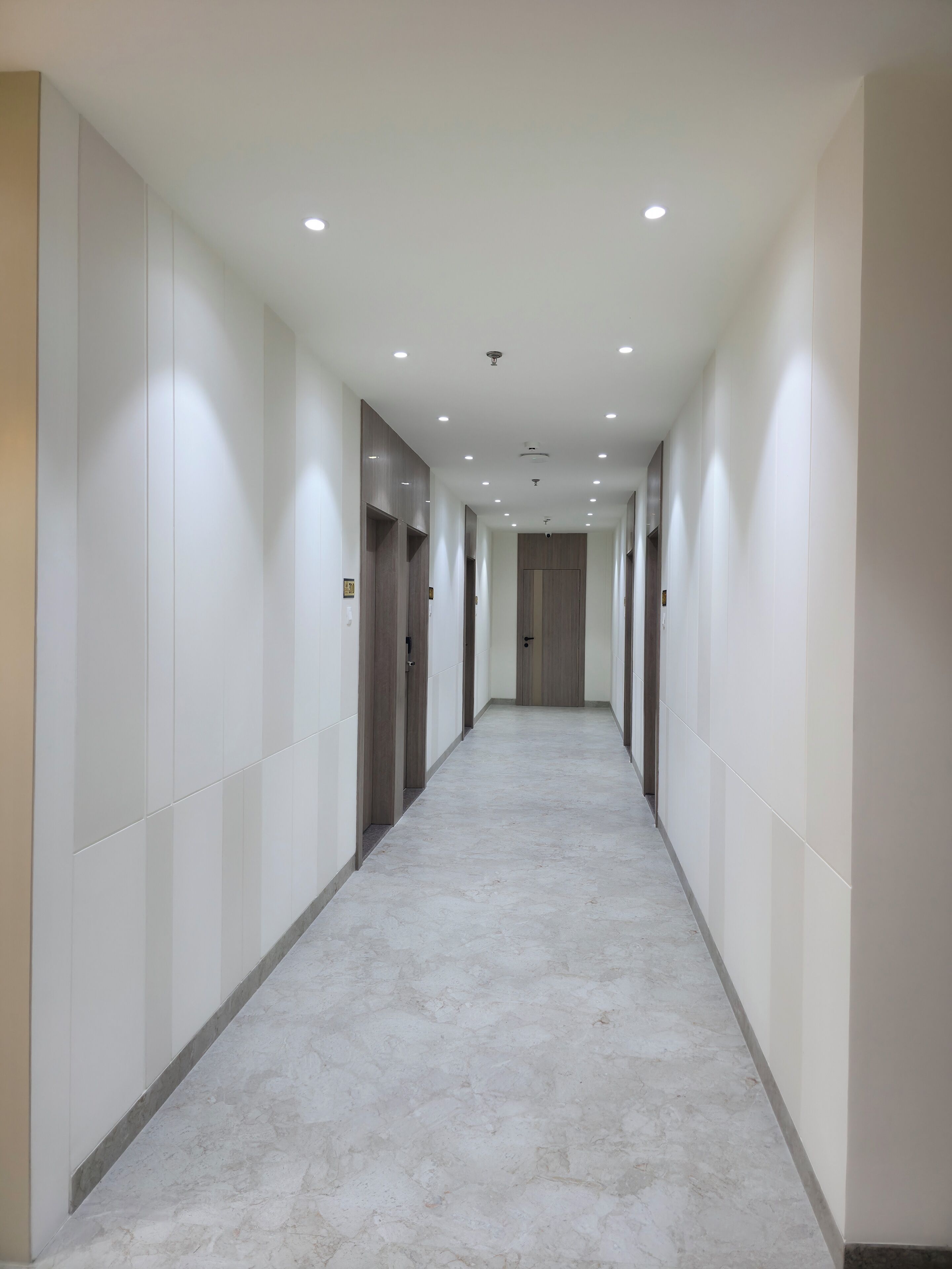 A long, narrow hallway with white walls and a marble floor.