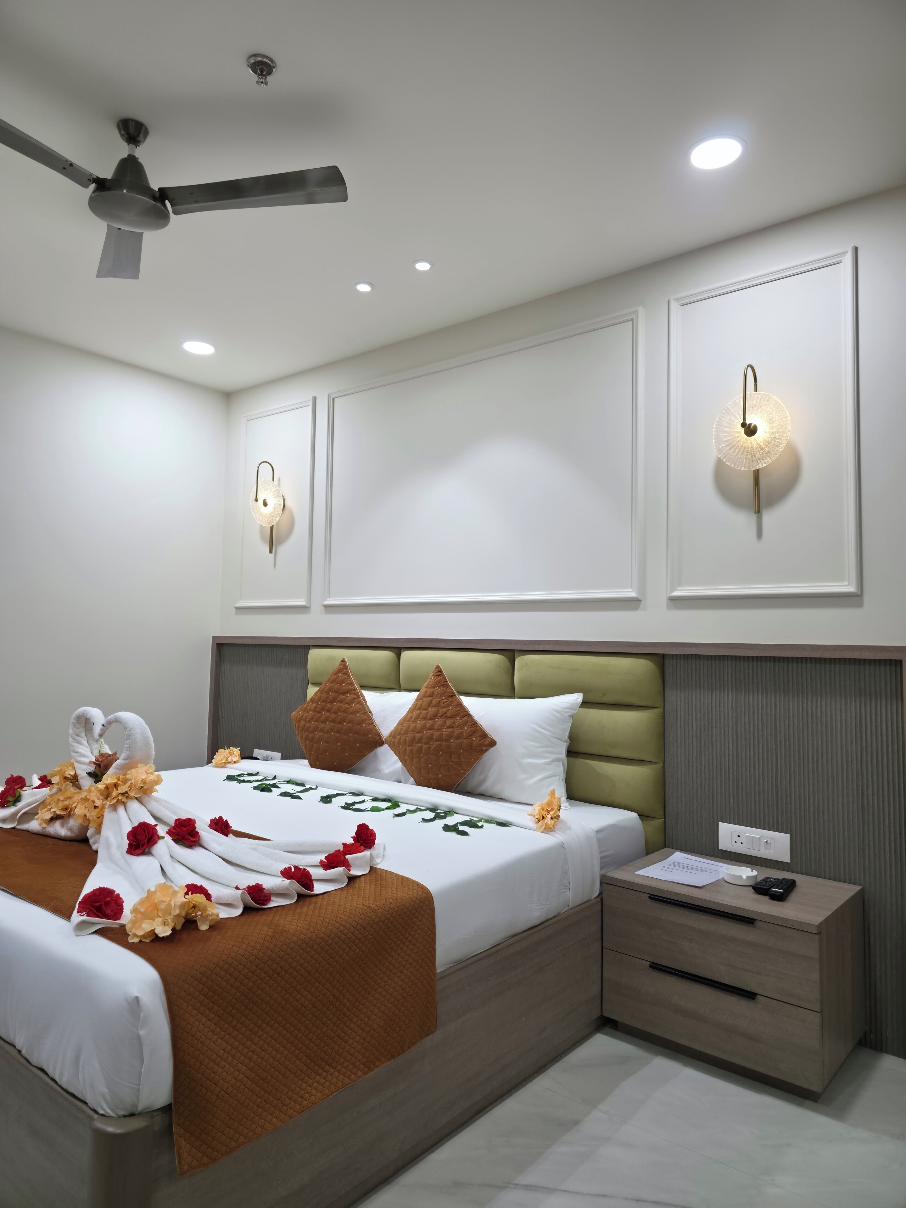 A modern hotel room with a neatly made bed, a bedside table with a lamp, and a ceiling fan.