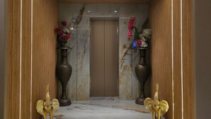 A marble-floored corridor with an elevator, flanked by wooden panels and two large vases with flowers. - Bawa Hotel (Kanpur)