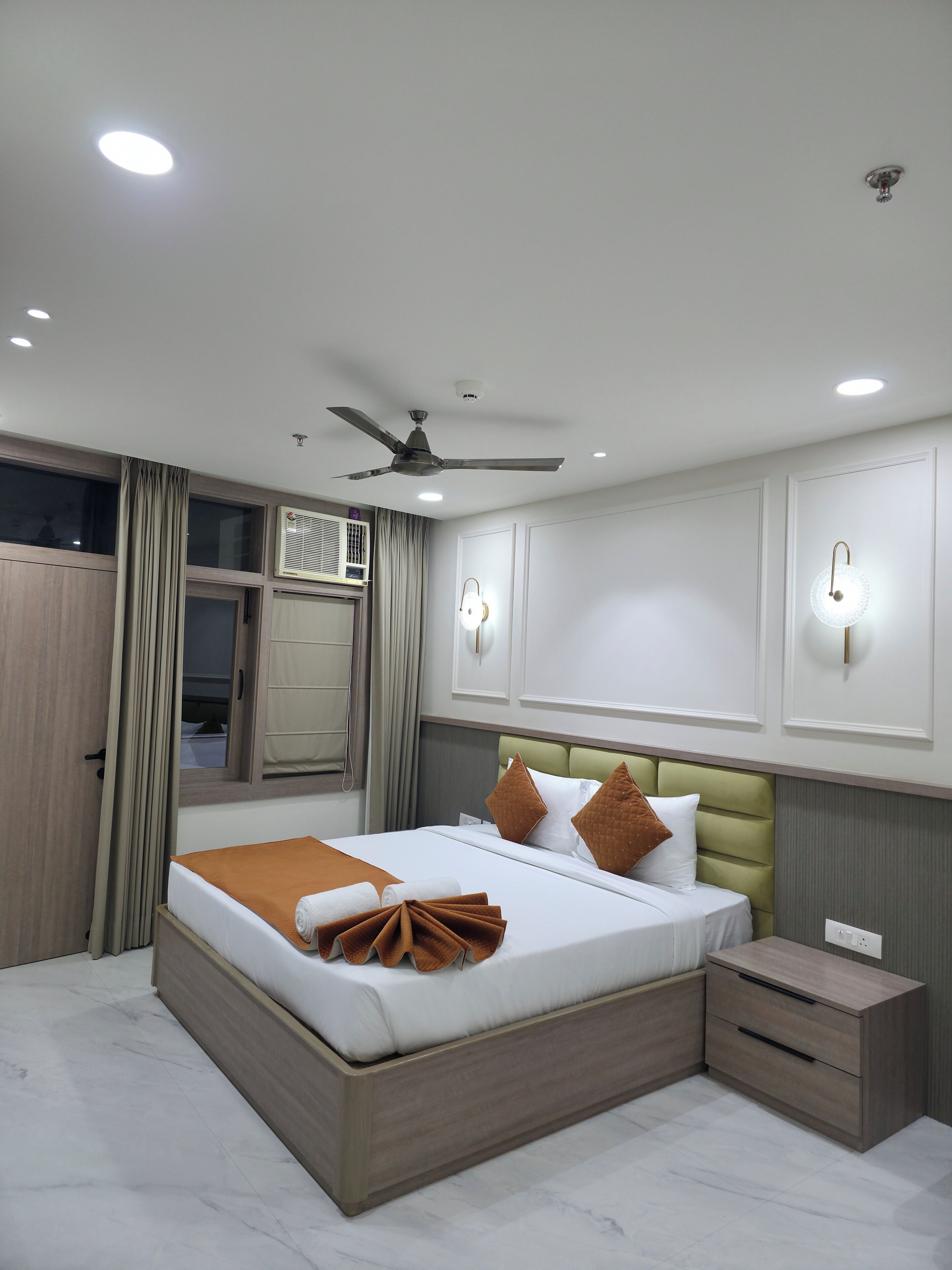 Camera d'albergo moderna con un letto grande, una ventola a soffitto, illuminazione a incasso, un comodino e un armadio.