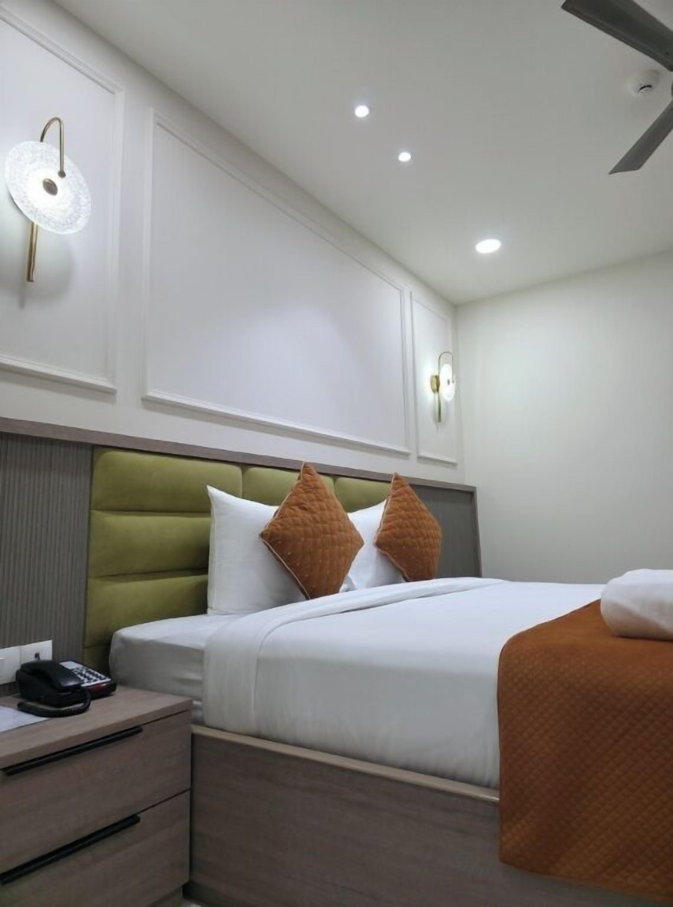 A hotel room with a bed, a bedside table, and a wall-mounted light fixture.