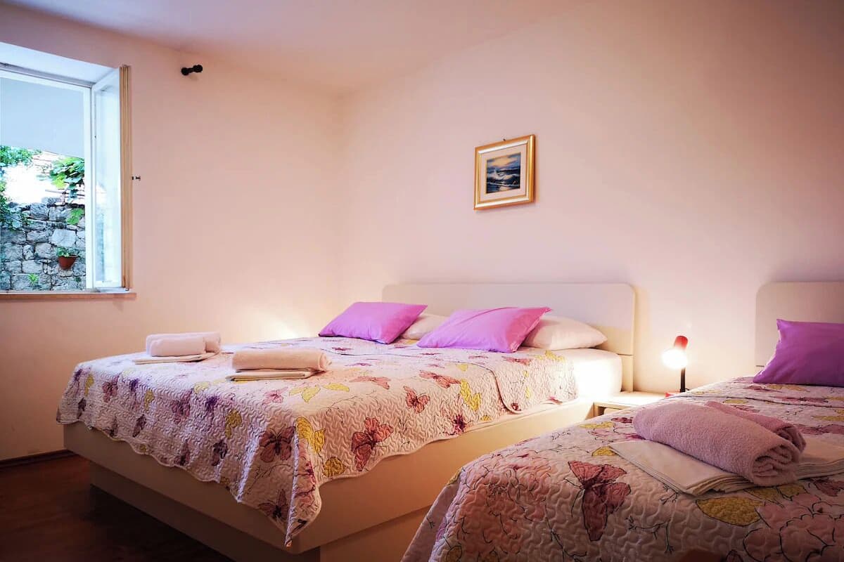 A bedroom with two beds, each with a floral bedspread and pink pillows. There is a small framed picture on the wall above the beds.