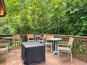 An outdoor deck with wooden chairs and tables, surrounded by lush greenery. - Indoor Waterpark Escape w/ Games & Firepit (Mc Gaheysville)