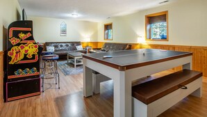 A room with a ping pong table, a sofa, a lamp, and a window. - Indoor Waterpark Escape w/ Games & Firepit (Mc Gaheysville)