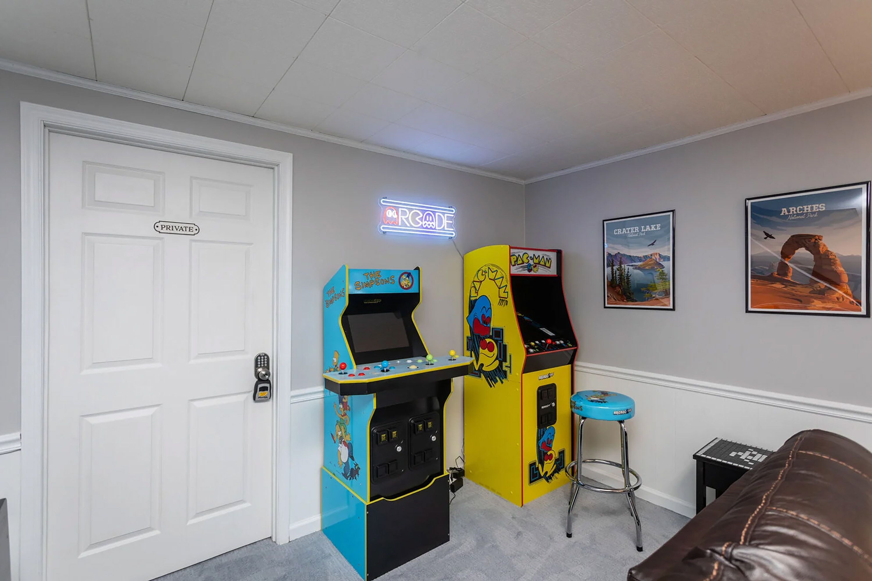 A room with arcade machines, a neon sign, and framed pictures on the wall.
