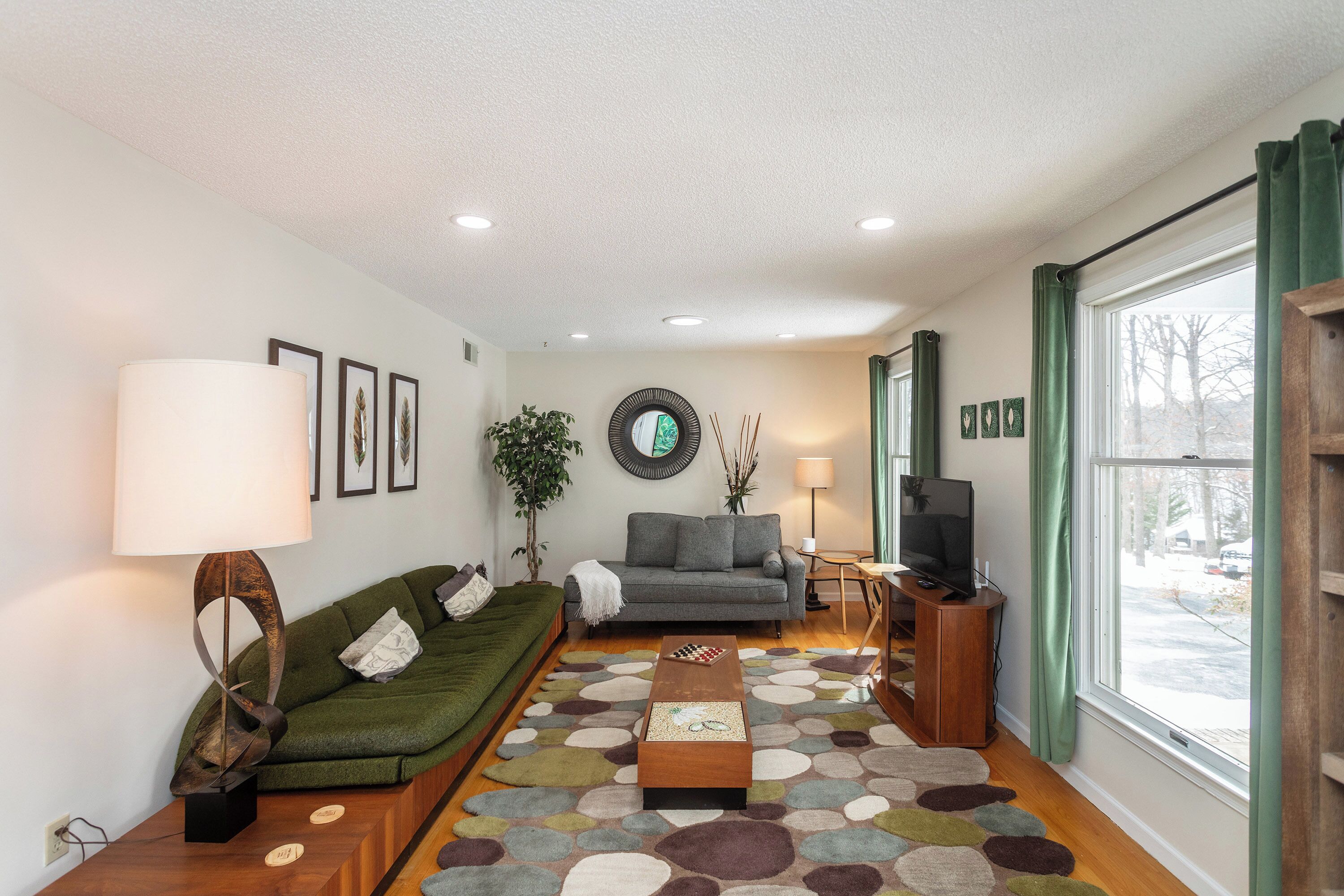 A living room with a sofa, a coffee table, a TV, and a large window with curtains.