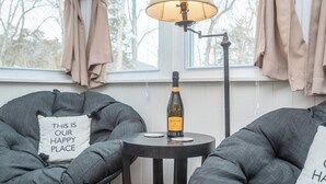 Un rincón acogedor con dos sillones grises, una mesita redonda con una botella de vino y una lámpara.