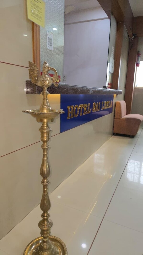 A reception desk with a sign reading "HOTEL SAI BELLA" and a traditional brass lamp in front. - Hotel Sai Leela (Ambernath)