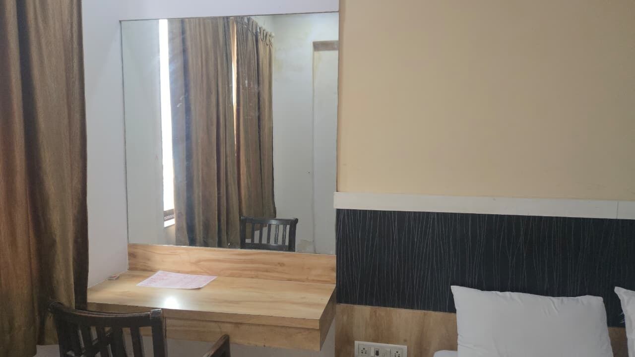 A hotel room with a wooden desk, a mirror, a bed with white pillows, and a black headboard.
