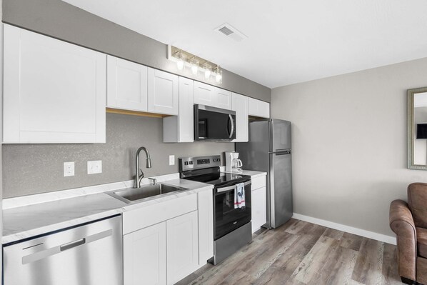 A modern kitchen with white cabinets, stainless steel appliances, and a wooden floor.