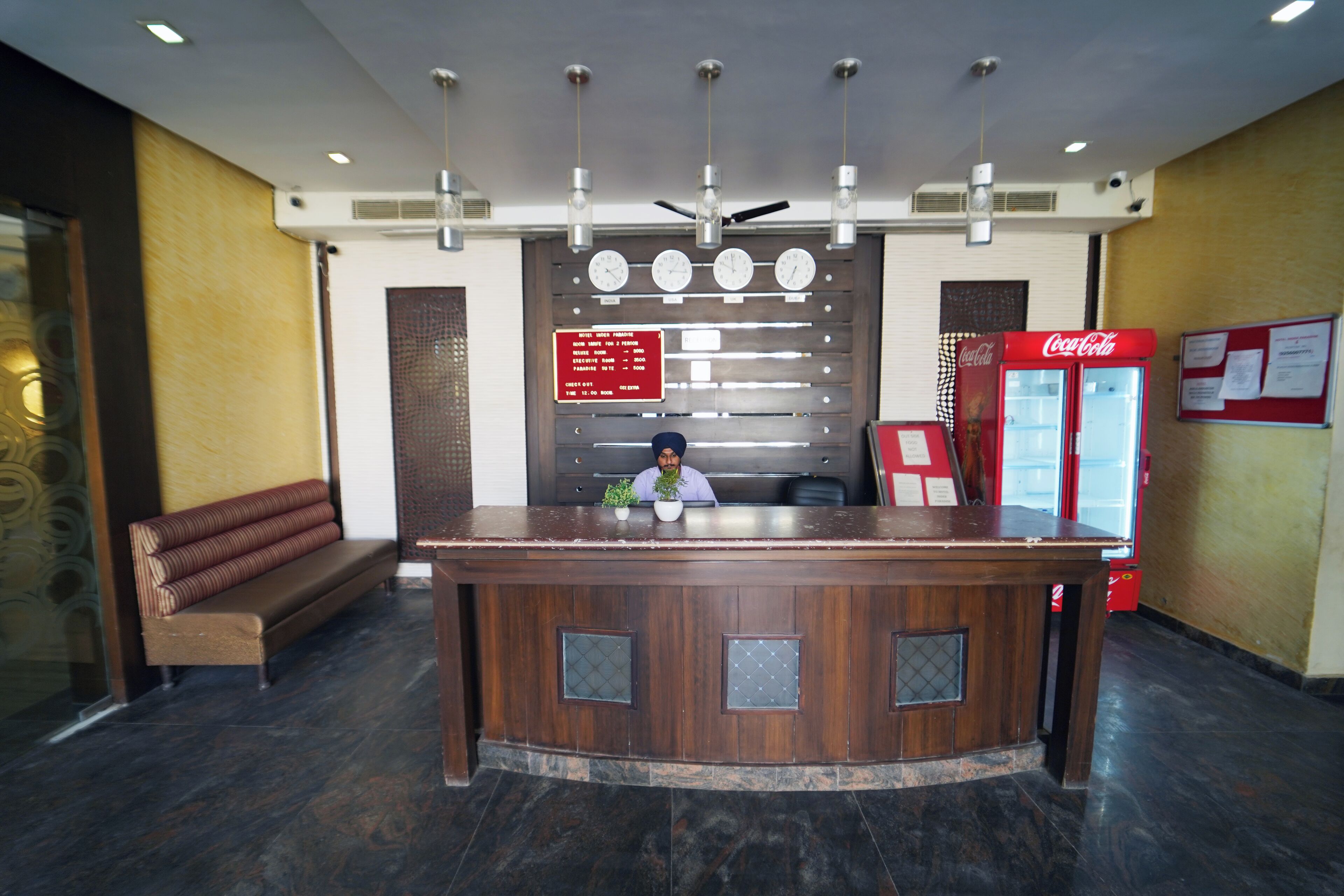 A reception desk with a clock, a Coca-Cola refrigerator, and a bench.