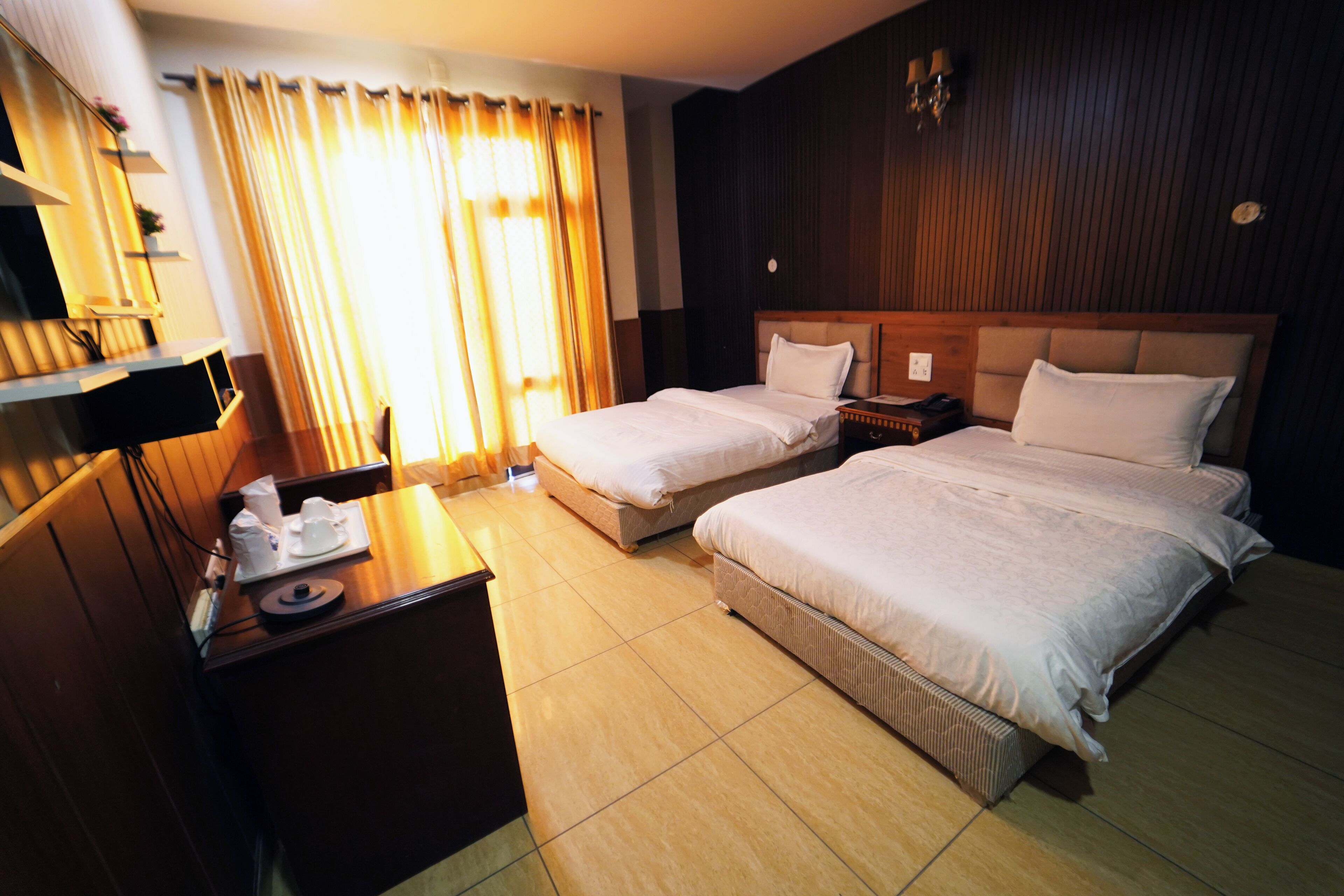 A hotel room with two beds, a desk, a chair, and a window with curtains.