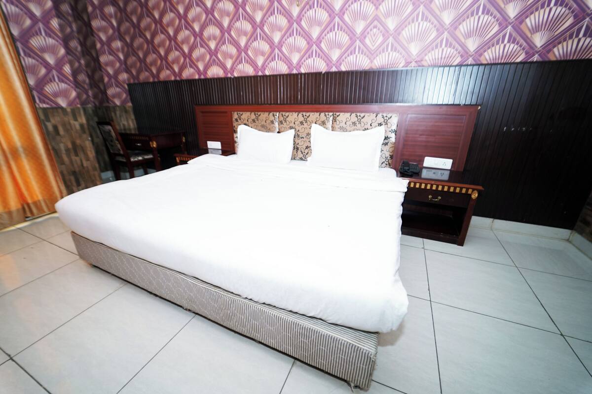 Uma cama grande com cabeceira de madeira, duas mesas de cabeceira e parede estampada.