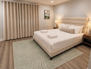 Cama bem arrumada com cobertura acolchoada, abajur e quadro na parede.