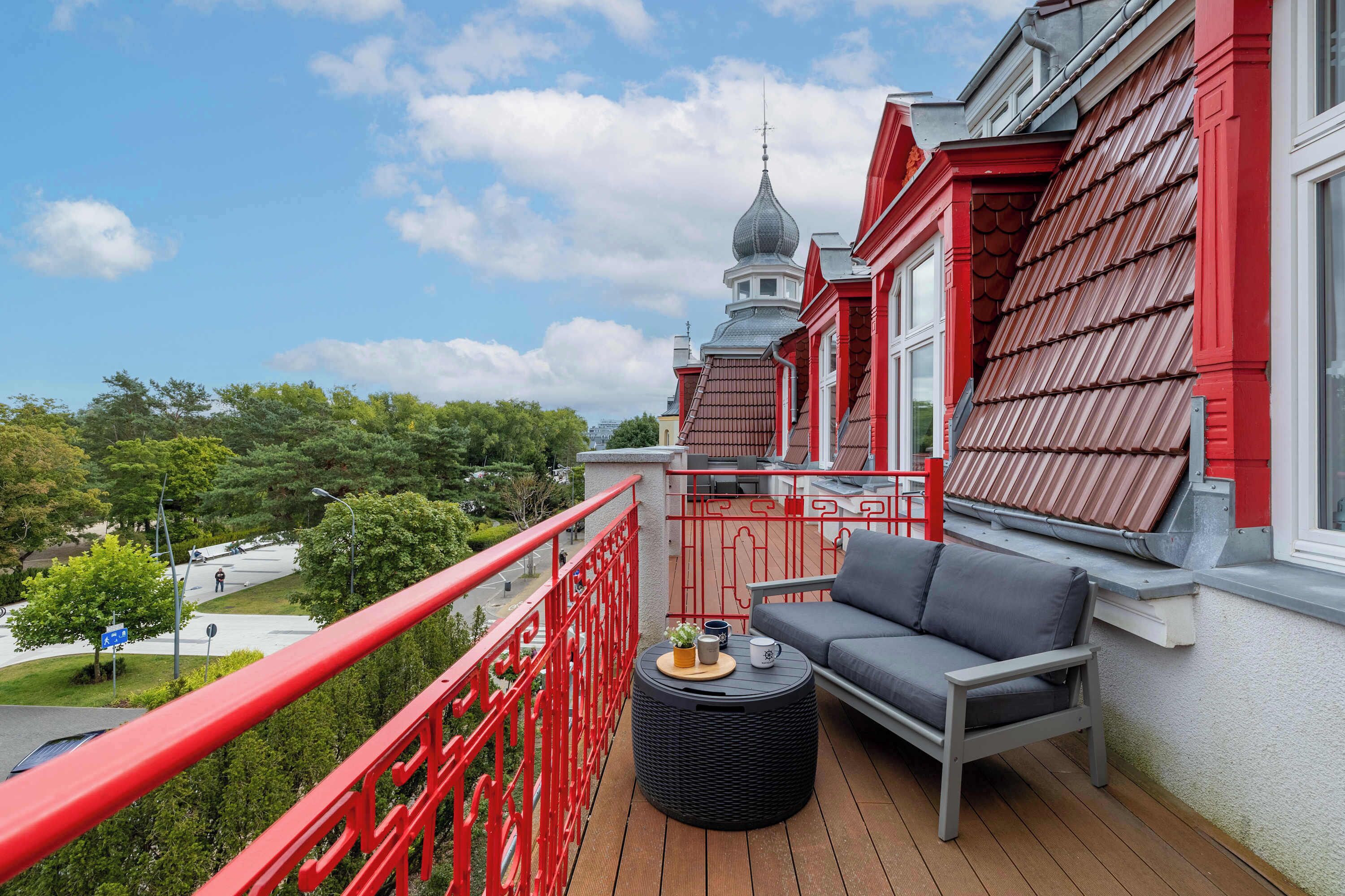 A balcony with a red railing, a grey sofa, and a small round table with a plant and a mug.