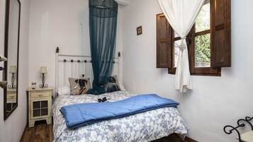 Un dormitorio con cama, mesita de noche, ventana con cortinas y suelo de madera.