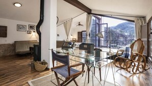 Un amplio espacio habitable con una mesa de vidrio, sillas de mimbre, un sofá y vistas a un paisaje montañoso.