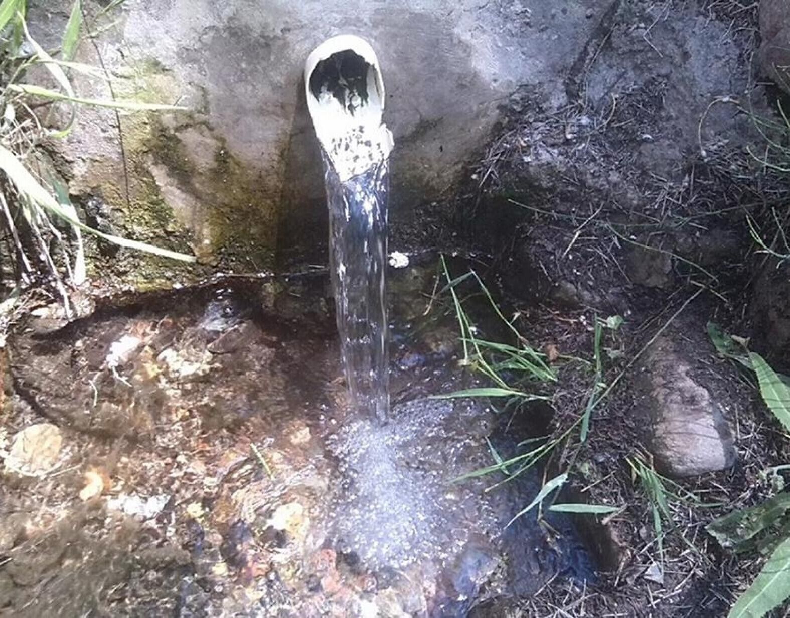 Luonnonmukainen vesialue, jossa kirkas vesi virtaa kivirakenteesta, ja aluetta ympäröivät kivet ja kasvillisuus.