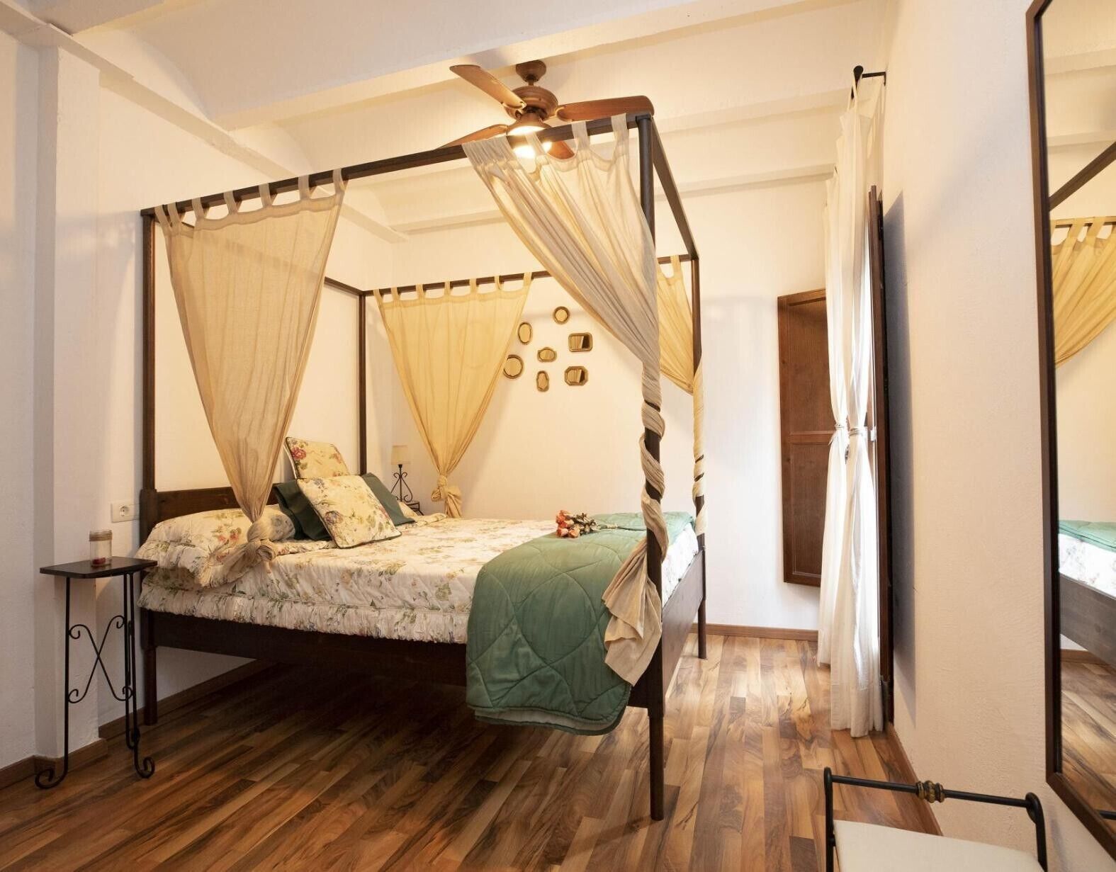 Una cama con dosel sobre cuatro columnas, suelo de madera y una mesita de noche.