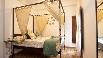 Una cama con dosel sobre cuatro columnas, suelo de madera y una mesita de noche.
