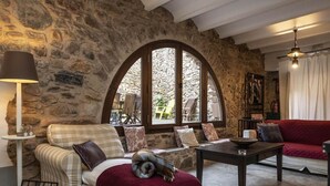 Una habitación acogedora con pared de piedra, un amplio ventanal de arco, un sofá, una mesa y una lámpara.