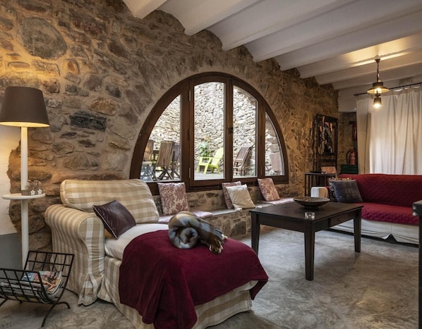 A cozy room with a stone wall, a large arched window, a sofa, a table, and a lamp.