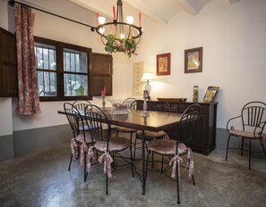 A dining area with a wooden table, six chairs, a chandelier, and a window with curtains.