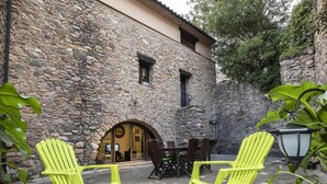 Un edificio de piedra con una mesa de madera y dos sillas verdes brillantes al frente.
