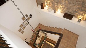 Una escalera con barandilla de madera, un muro de piedra con iluminación decorativa y un espejo que refleja la habitación de abajo.