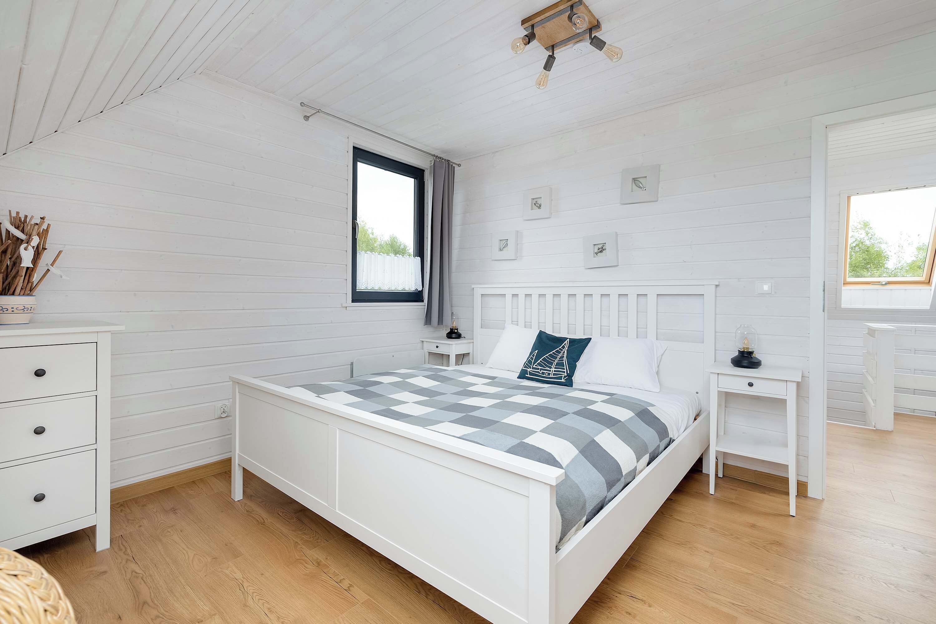 A bedroom with a bed, white dresser, bedside tables, and a window with curtains.
