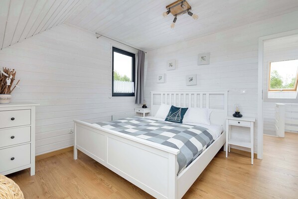 A bedroom with a bed, white dresser, bedside tables, and a window with curtains.