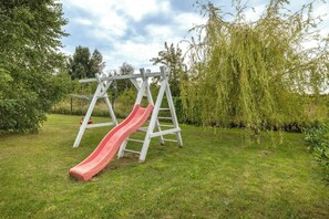 Un parque infantil con un tobogán rojo y un columpio blanco en un área verde con árboles.
