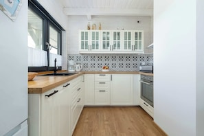 Eine kompakte Küche mit weißen Schränken, einer Holz Arbeitsplatte, einer gemusterten Spritzschutzleiste und einem eingebauten Backofen.
