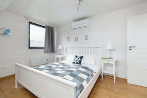 Ein Schlafzimmer mit einem Bett, Nachttischen, einem Fenster und einer Klimaanlage.