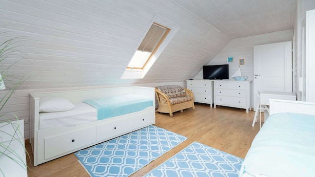 Une chambre avec un plafond en pente, un lit, une télévision, une commode et une chaise.
