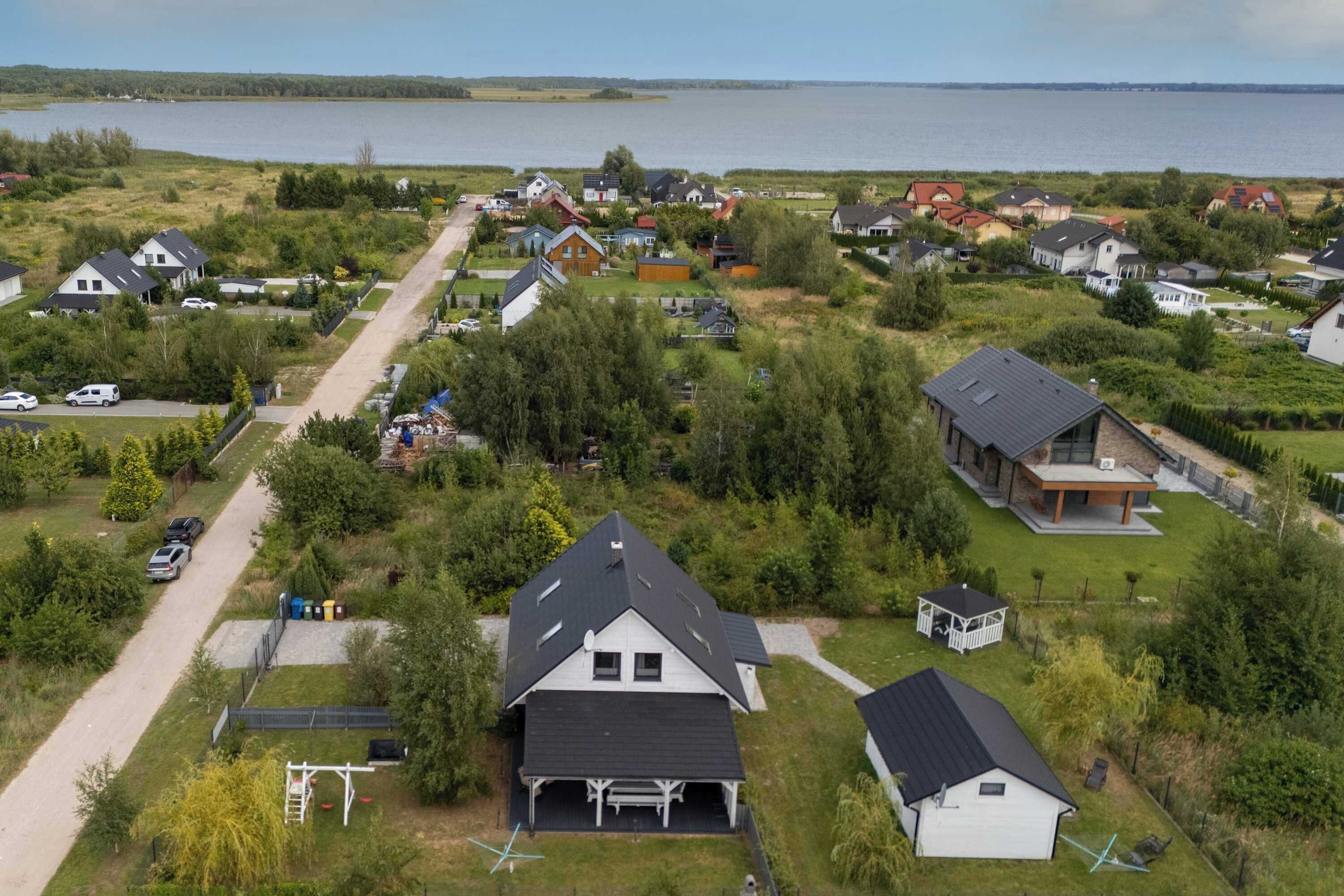 An aerial view of a residential area with houses, a road, and a body of water in the background.