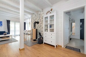 A modern living room with a stone wall, wooden flooring, a white cabinet with glass doors, and a dining area with a table and chairs.
