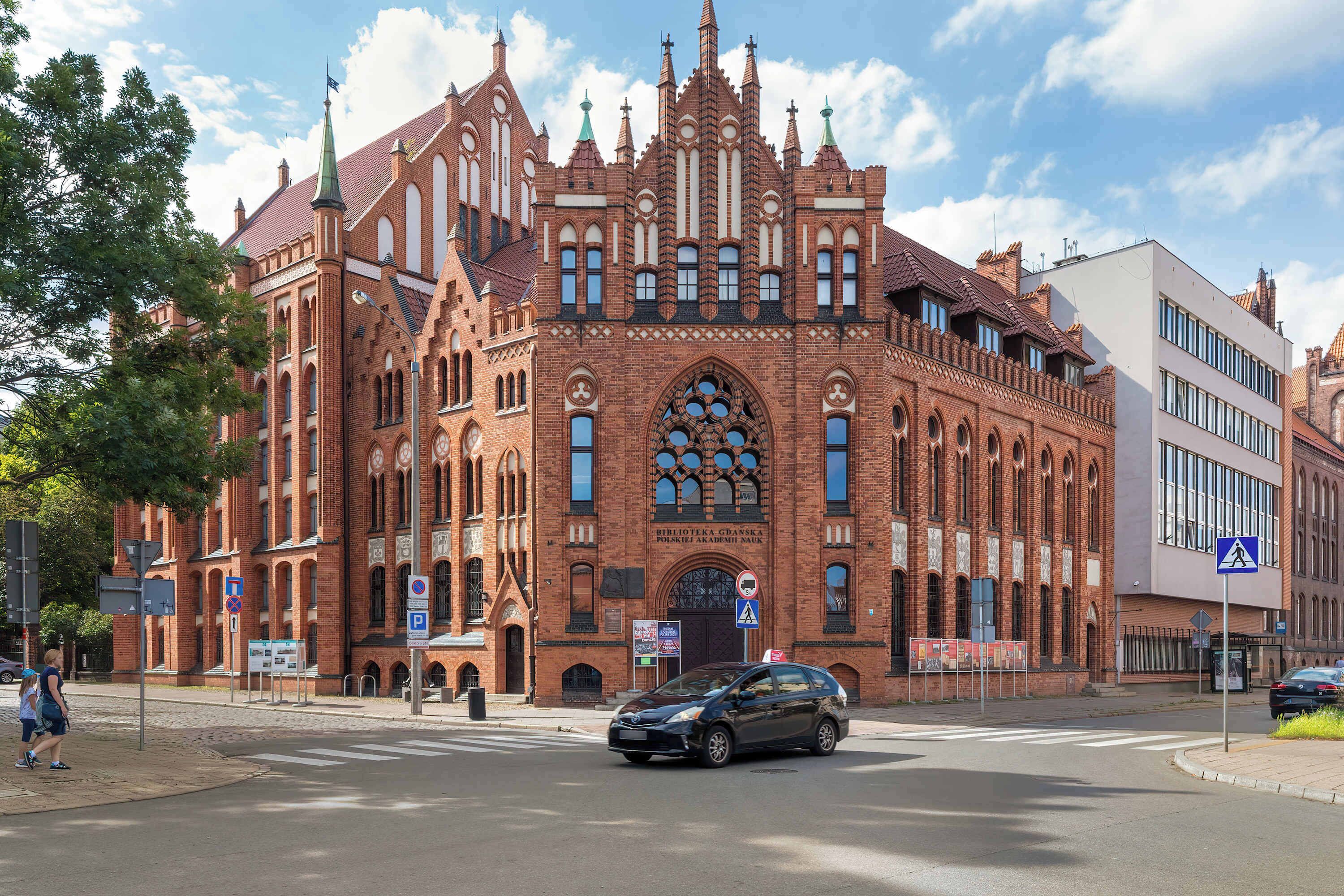 A historic red brick building with Gothic architectural elements, a large arched entrance, and a modern extension.
