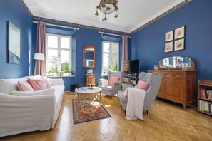 A living room with a white sofa, a checkered armchair, a wooden cabinet, and a television.