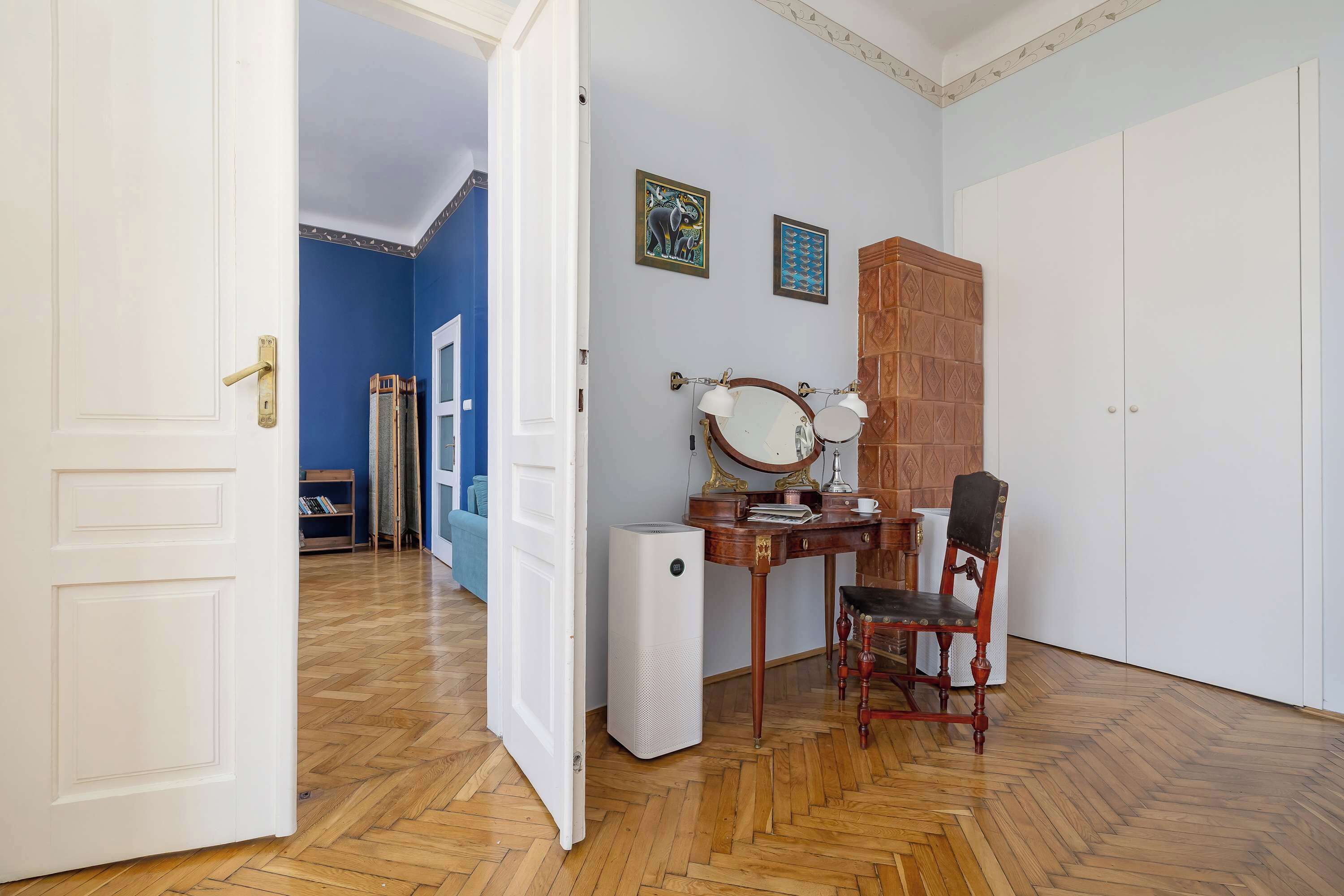 A room with a wooden herringbone floor, a desk with a mirror, a chair, and a wardrobe.