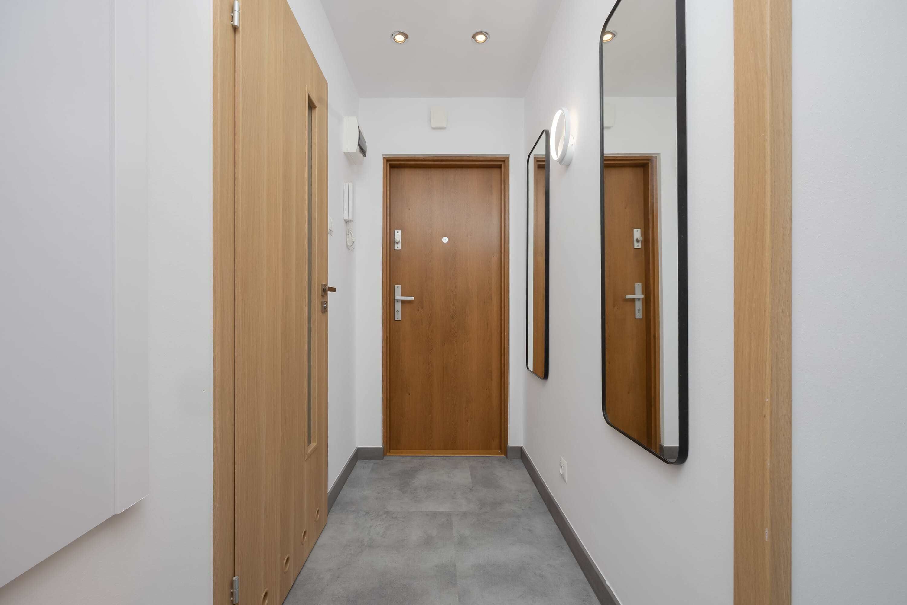Ein Flur mit einer Holztür am Ende, einem Spiegel an der Wand und einem Lichtschalter über der Tür.