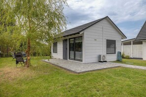 Ein kleines, eingeschossiges Haus mit einer Veranda, einem Rasen und einem Baum.